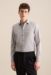 Lichtgrijze blouse met lange mouwen en een button-down kraag, voorzien van subtiele streepjes en donkere knopen, gecombineerd met zwarte trousers.