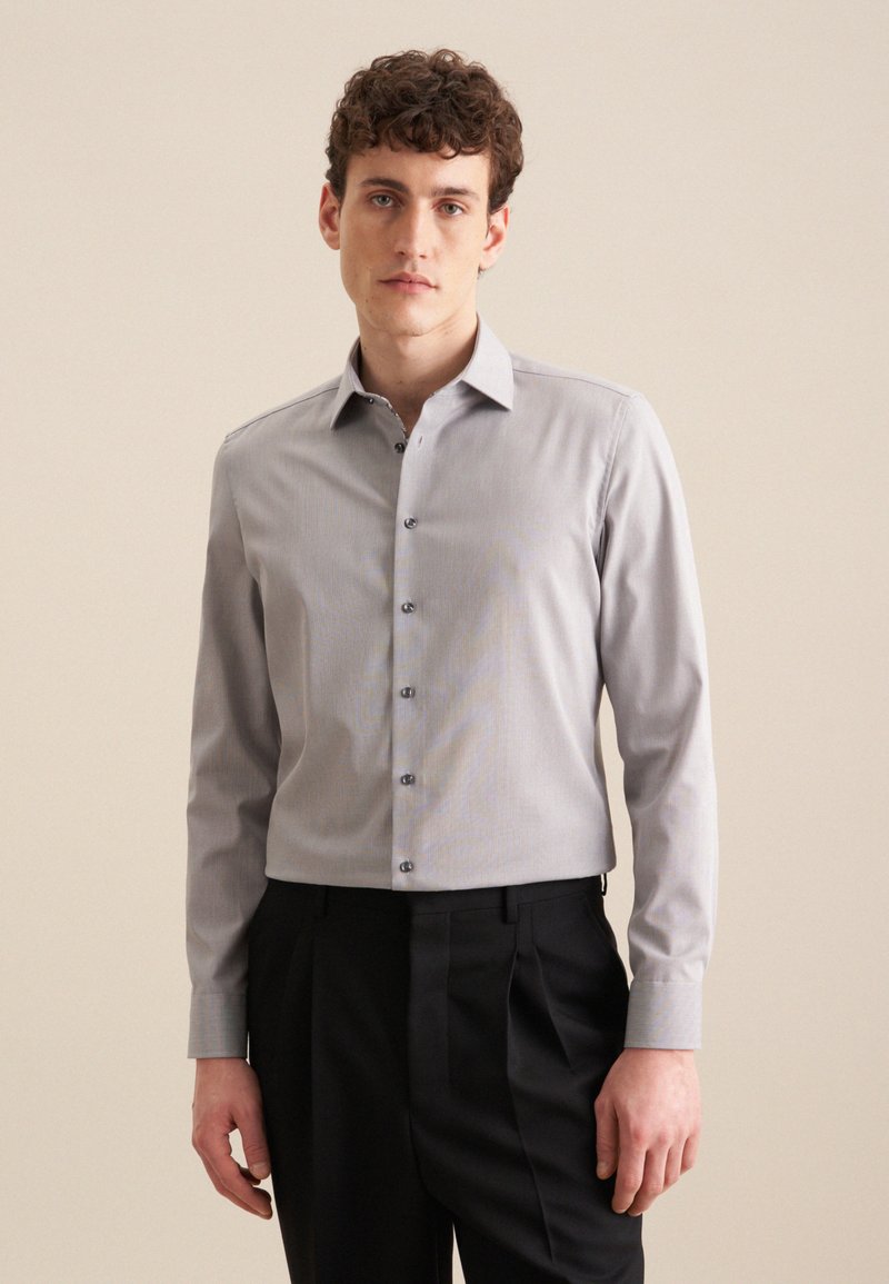 Lichtgrijze blouse met lange mouwen en een button-down kraag, voorzien van subtiele streepjes en donkere knopen, gecombineerd met zwarte trousers.