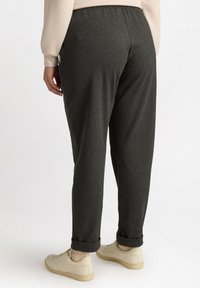 Charcoal grijze joggers met een losse pasvorm, elastische tailleband en opgerolde manchetten, gecombineerd met lichtbeige sneakers. Glad stofoppervlak.