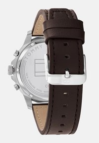 Montre avec bracelet en cuir brun, dotée d'un boîtier en acier inoxydable, avec une boucle en argent et un logo de marque gravé à l'arrière. Design résistant à l'eau.