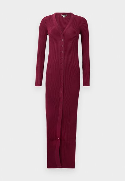 Burgundy ribbed long cardigan with a V-neck, full-length sleeves, and a front button closure. Features a slit at the hem for movement.