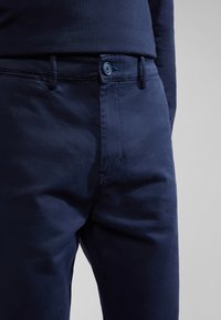 Pantaloni di cotone blu navy con una texture liscia, dotati di chiusura con bottone e cuciture in vista, che mettono in risalto un design di vestibilità classica.