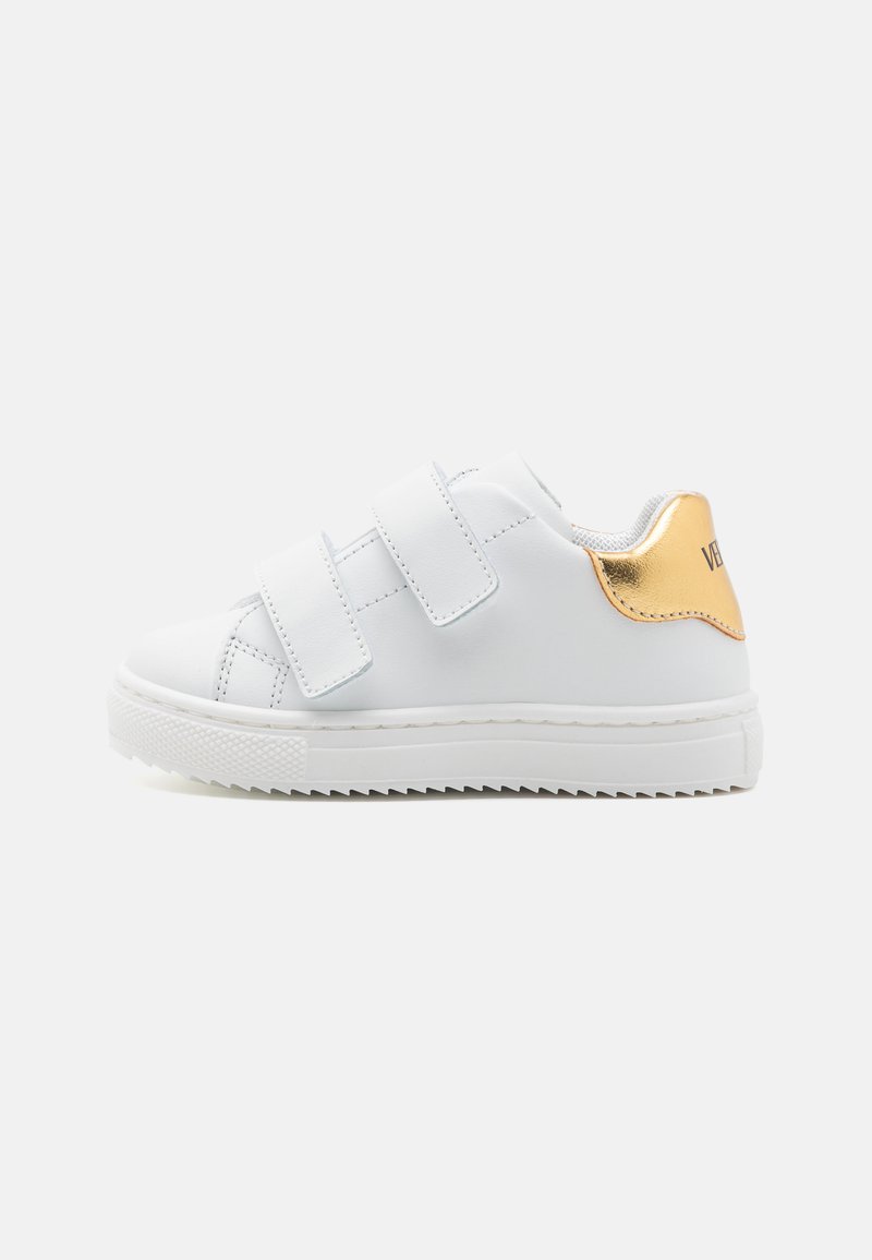 White sneaker with velcro straps, textured rubber sole, and a metallic gold accent on the heel. Smooth synthetic upper material.