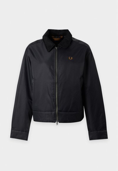 Veste noire zippée avec un col doux et un petit logo doré brodé sur la poitrine gauche, présentée sur un fond clair uni.