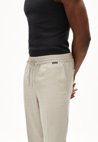 Licht beige linnen broek met een elastische tailleband en trekkoord. Beschikt over zijzakken en een klein merkembleem dat op de tailleband is gestikt.