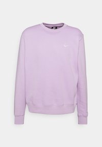 Sudadera púrpura con cuello redondo, mangas largas y puños acanalados. Presenta un pequeño logo blanco de Nike en el pecho y una textura suave.