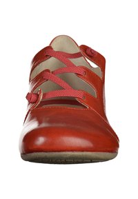 Zapato de cuero rojo con punta redondeada, con tiras entrecruzadas y acentos circulares. Superficie lisa con una suela flexible.