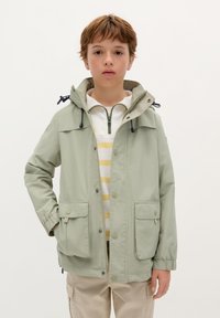 Lichtgroene windbreaker jas met capuchon, voorzien van twee voorzakken, elastische manchetbanden en een ritssluiting over een gestreept shirt.