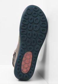 Skosula i grått gummi med ett strukturerat mönster. Den har cirkulära utskärningar och varumärket "CAMPER" i rött på en blå bakgrund.