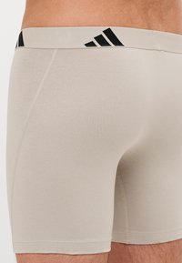 Calções desportivos bege com um design ajustado. Feitos de um tecido suave, apresentam uma cintura elástica preta com marca e costuras planas para conforto.