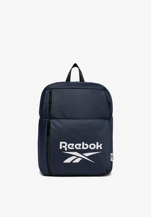 Mochila Reebok azul marino con gran bolsillo delantero con cremallera, cremalleras negras, asa de transporte y logo blanco de Reebok centrado en el bolsillo delantero.