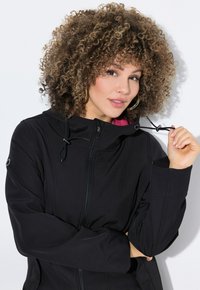 Veste à capuche noire avec une fermeture éclair à l'avant, dotée d'une doublure rose, de cordons de serrage ajustables et d'une texture lisse et élégante.