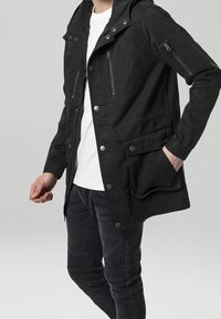 Giacca nera con cappuccio, dotata di tasche con zip sui lati e sul petto. Presenta una chiusura a scatto frontale, tessuto testurizzato e una vestibilità rilassata. Abbinate a jeans scuri.