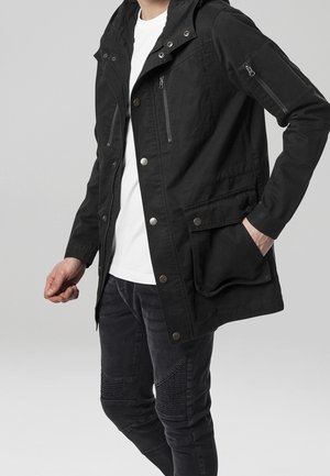 Veste à capuche noire avec poches zippées sur les côtés et la poitrine. Comprend une fermeture à pression à l'avant, un tissu texturé et une coupe décontractée. Associée à un jean foncé.