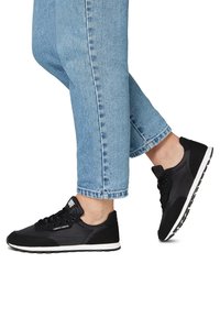 Sneakers neri con una tomaia sintetica liscia e accenti in suede, suola bianca, punta rotonda e design con lacci. Indossati con jeans azzurri chiari.
