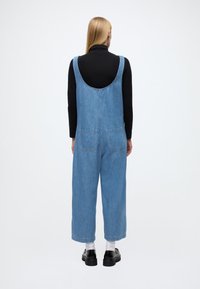 Lyseblå denimdongeribukse med lav rygg, vide ben og to baklommer. Brukt over en svart langermet topp og hvite sokker. Sorte sko.