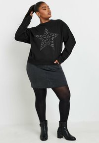 Svart sweatshirt med en stjärndesign i leopardtryck och strass, parat med en denimkjol och svarta strumpbyxor. Svarta klackade ankelskons.