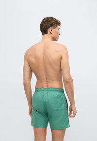 Zelené plavkové šortky z ľahkej látky, s pružným pásom, bočnými pruhmi a zadným vreckom s jemnou textúrou.