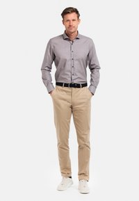 Lichtgrijs gestreept overhemdo gecombineerd met beige chinos. Witte sneakers maken de outfit compleet, met een donkere riem.