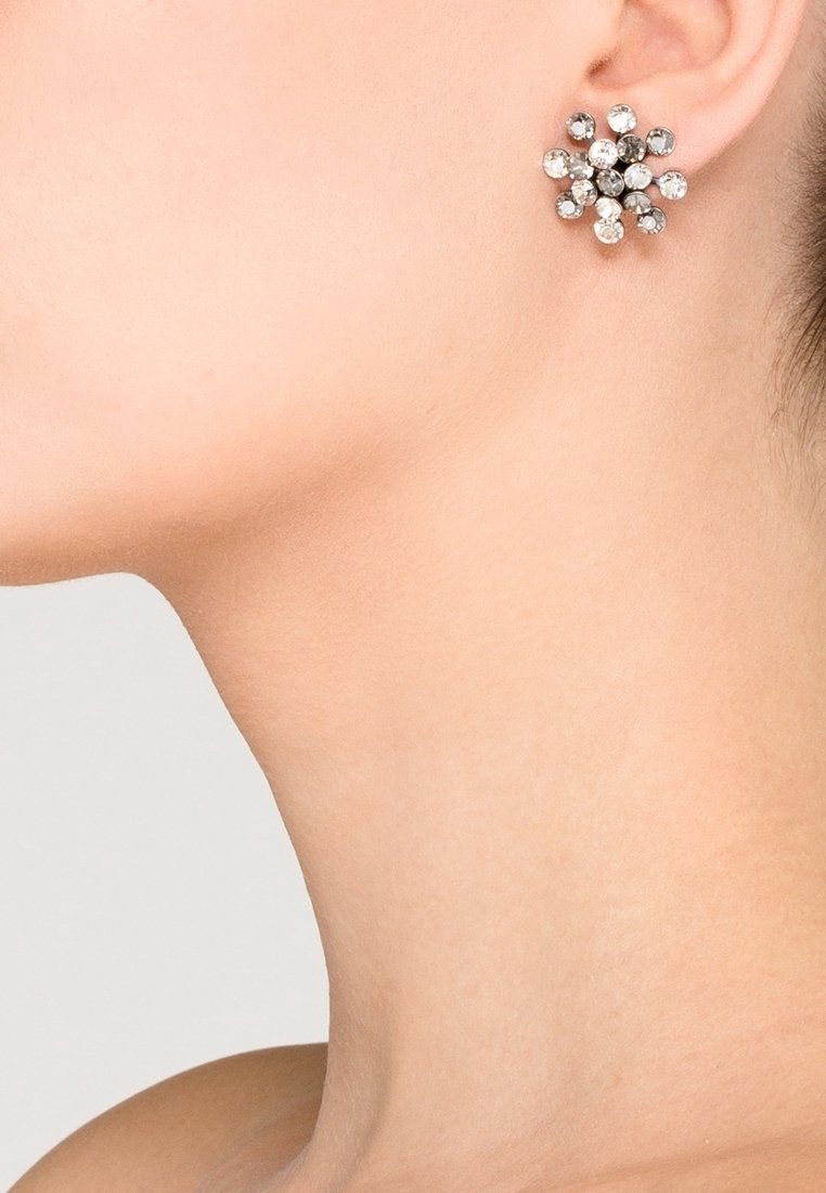 Cou et ligne de la mâchoire d'une femme avec un gros plan d'une boucle d'oreille clou argentée en forme de fleur avec des pierres précieuses transparentes.