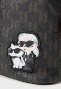 Patch de dessin animé d'une personne aux cheveux blancs en costume noir et lunettes de soleil, se tenant à côté d'un chat blanc également équipé de lunettes de soleil noires, sur un sac à motif sombre.