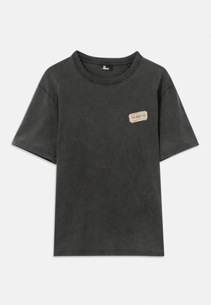 Must välja lühikese varrukaga ümmarguse kaelusega T-särk, millel on vasakul rinnal väike beež ristkülikukujuline kleebis, millel on tekst "THE KOOPLES".