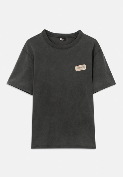 T-shirt preto de manga curta com decote redondo, apresentando um pequeno retângulo bege com a inscrição "THE KOOPLES" no lado esquerdo do peito.