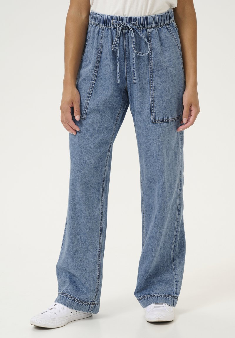 Gaiši zili džinsu bikses ar brīvu piegriezumu, elastīgu jostu un aukliņu, ar priekšējām papildus kabatām un izšuvuma akcentiem.