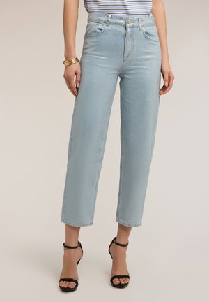 Femme portant un jean court taille haute bleu clair avec un haut rayé, des bracelets en or et des sandales noires à talons hauts, debout.