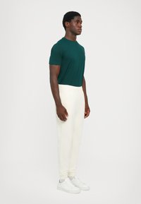Green short-sleeve t-shirt, white elastic-waist joggers, and white sneakers. Simple design, smooth texture, and relaxed fit.