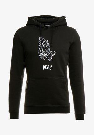Schwarzer Hoodie mit einer Frontgrafik von betenden Händen in Weiß, versehen mit dekorativen Kettendetails. Der Text darunter lautet "pray" (beten). Weiches, texturiertes Material.