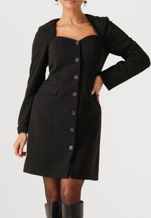 Zwarte jurk gemaakt van gestructureerde stof, met lange mouwen, een sweetheart halslijn, een knoopsluiting aan de voorkant en zijzakken.