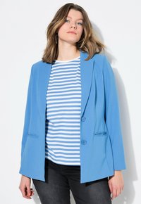 Blazer azul claro hecho de una tela suave con solapas de muesca, botones frontales y un bolsillo en el pecho, combinado con una camiseta a rayas azul y blanca.