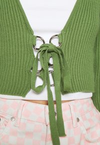 Zelený žebrovaný pletený krátký kardigan s výstřihem do V a stříbrnými kruhovými ozdobami vpředu, s vázačkami a texturovaným povrchem.