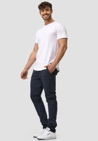 White short-sleeve t-shirt paired with dark navy pants and white sneakers. The pants feature side pockets and a slim fit design.