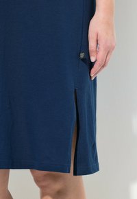 Tmavě modré bavlněné šaty s bočními rozparky na lemu, hladkou texturou a malou značkovou etiketou na levé straně.