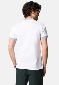 Biała koszulka polo z jasnoniebieskim akcentem na ribbrowanym kołnierzyku i rękawach, wykonana z miękkiego materiału, charakteryzująca się prostym, minimalistycznym designem.