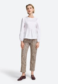 Witte langarmtop met verzamelde taille, gecombineerd met beige leopardprint broek en maroon schoenen. Eenvoudig, schoon ontwerp met contrasterende patronen.