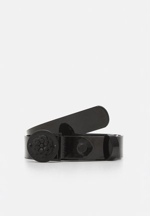 Czarny błyszczący pasek z okrągłą klamrą z tłoczonym kwiatowym wzorem i pętlą, zwinięty na białym tle.