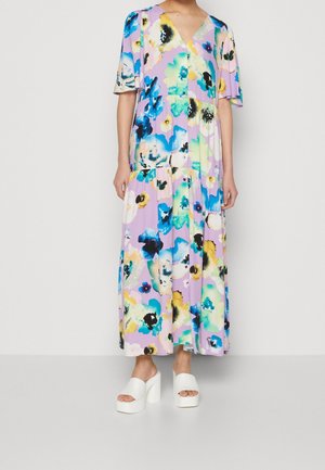 Sukienka w kwiatowy wzór w odcieniach różu, niebieskiego i zielonego; z dekoltem w kształcie litery V, krótkimi rękawami i warstwowym dołem. Uzupełniona białymi sandałami na platformie.