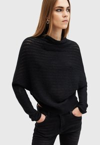 Maglione nero a maglia con collo a camicia e maniche lunghe e aderenti. Caratterizzato da un design testurizzato e a strati con una silhouette morbida. Abbinato a un paio di jeans scuri.