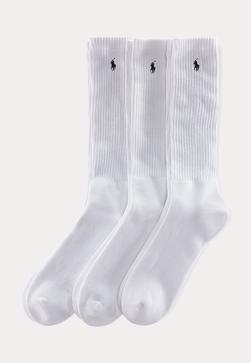 Trois chaussettes blanches à bord-côtes avec de petits logos noirs de joueur de polo près du haut, disposées côte à côte sur un fond uni.