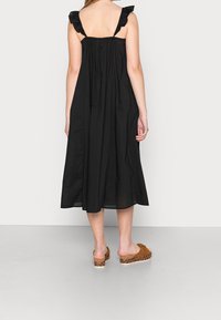 Robe midi noire avec bretelles volantées, dos froncé et tissu fluide. Portée avec des sandales à plateforme marron dotées d'une semelle à imprimé léopard.