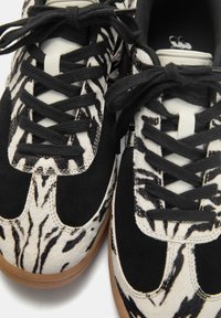 Sorte og hvide sneakers med en blanding af ruskind og dyreprint teksturer, med sorte snørebånd og en gummisål.