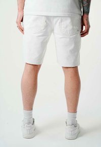 Shorts in denim bianco con orlo sfrangiato, dotati di tasche posteriori. Indossati con sneakers bianche e calze, che mostrano un look casual.