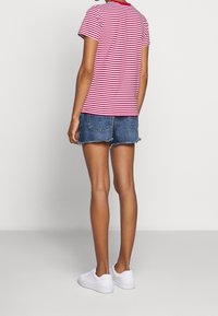 Czerwono-biała koszulka w paski, krótki rękaw, zestawiona z dżinsowymi szortami. Model nosi białe trampki, przedstawiony od tyłu.