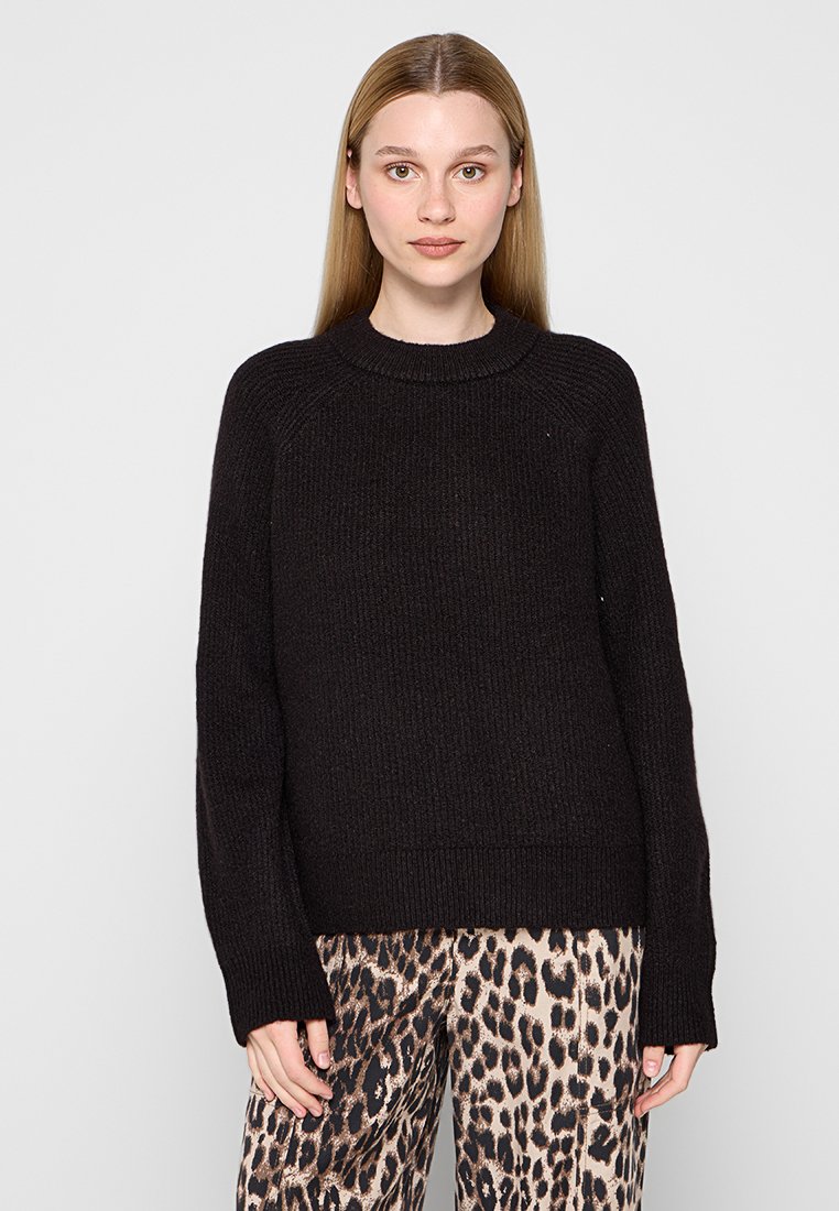 Maglione nero lavorato a maglia con collo rotondo, texture a costine e maniche lunghe, abbinato a pantaloni con stampa leopardata.