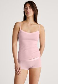 Lichtroze cami-top met dunne bandjes en een zacht gebogen halslijn, gecombineerd met bijpassende shorts met een subtiele uitsnijding. Gladde textuur.