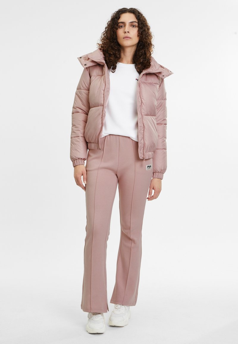 Giacca a vento rosa con cappuccio e chiusura a zip, abbinata a pantaloni della tuta coordinati con il logo Fila. Entrambi i capi sono realizzati in tessuto morbido.