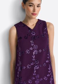Fioletowa sukienka bez rękawów z dekoltem w kształcie litery V, ozdobiona cekinami w różnych odcieniach fioletu, tworzącymi teksturowany, kwiatowy wzór.
